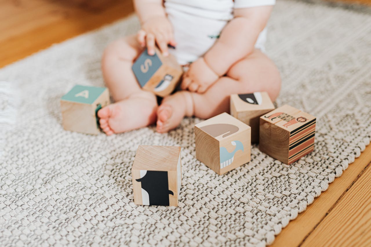 Adorable baby sitting on a rug and playing with colorful wooden blocks.